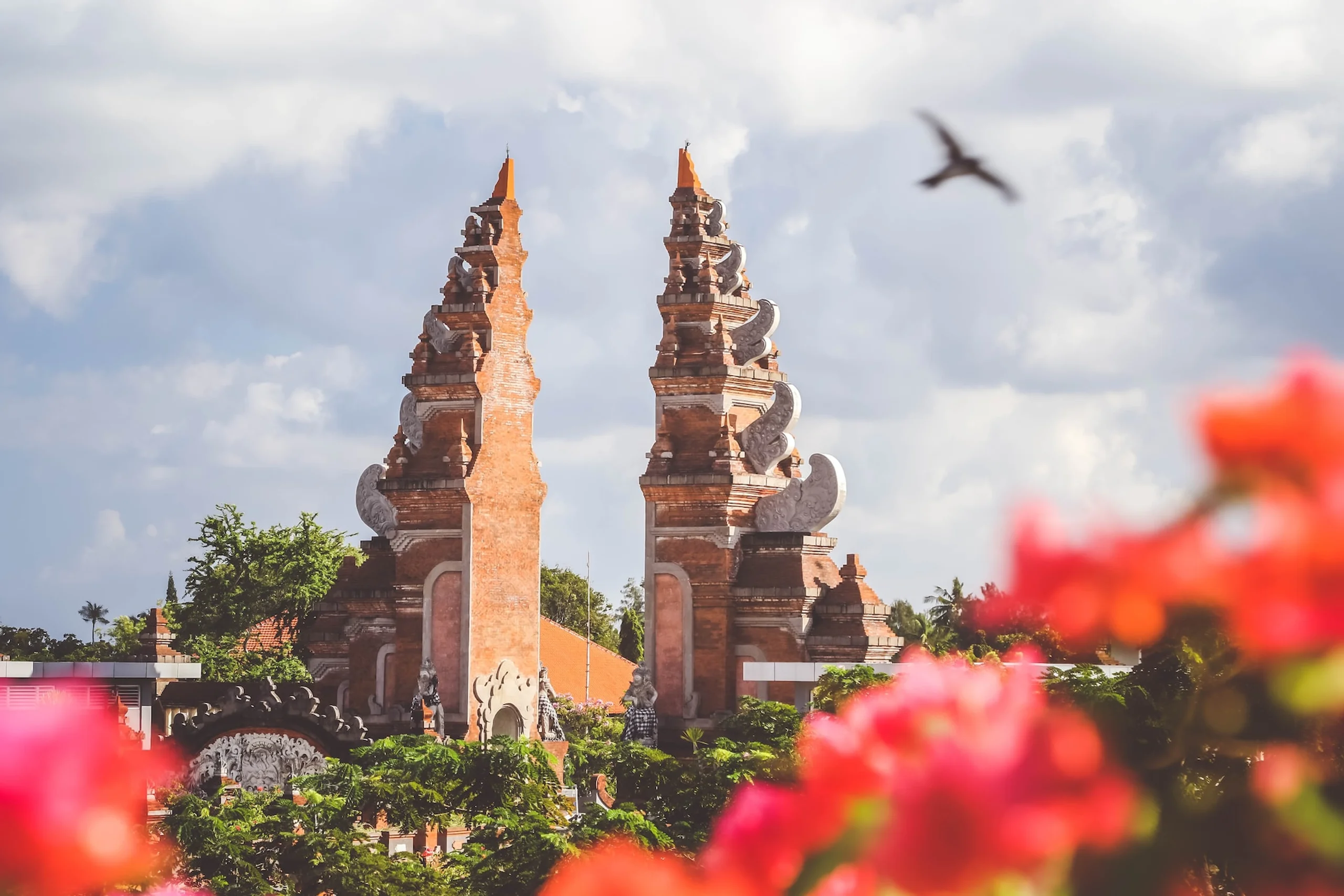 Temple gates surrounded by trees with bird flying in the sky