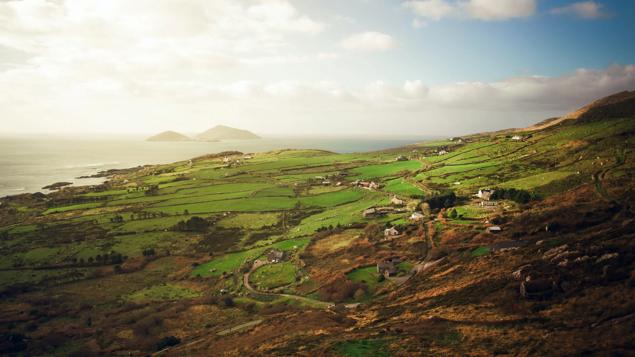 Green farm hill rolling into the ocean with two small mountain islands in the distance