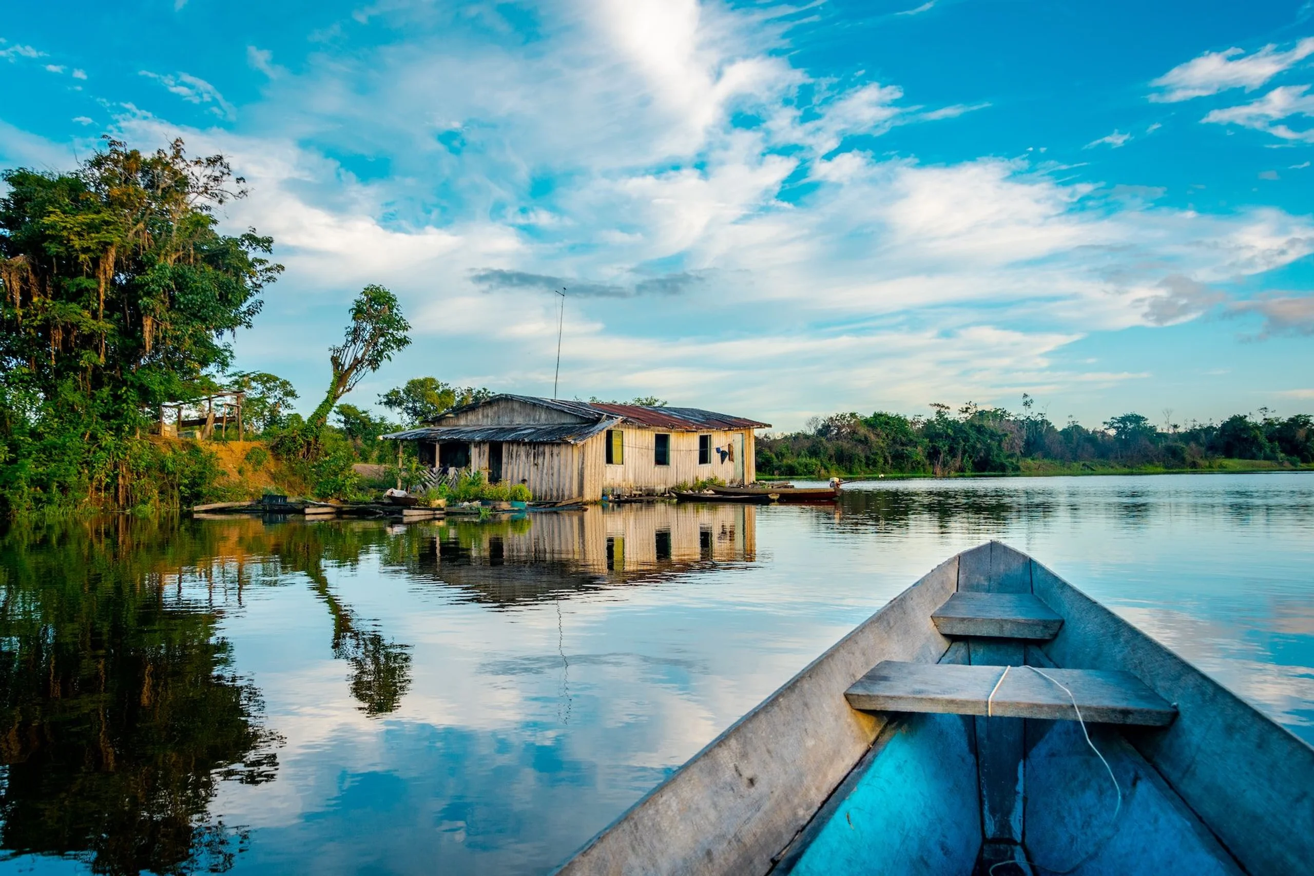 Bow of a canoe floating past a house on the Amazon river