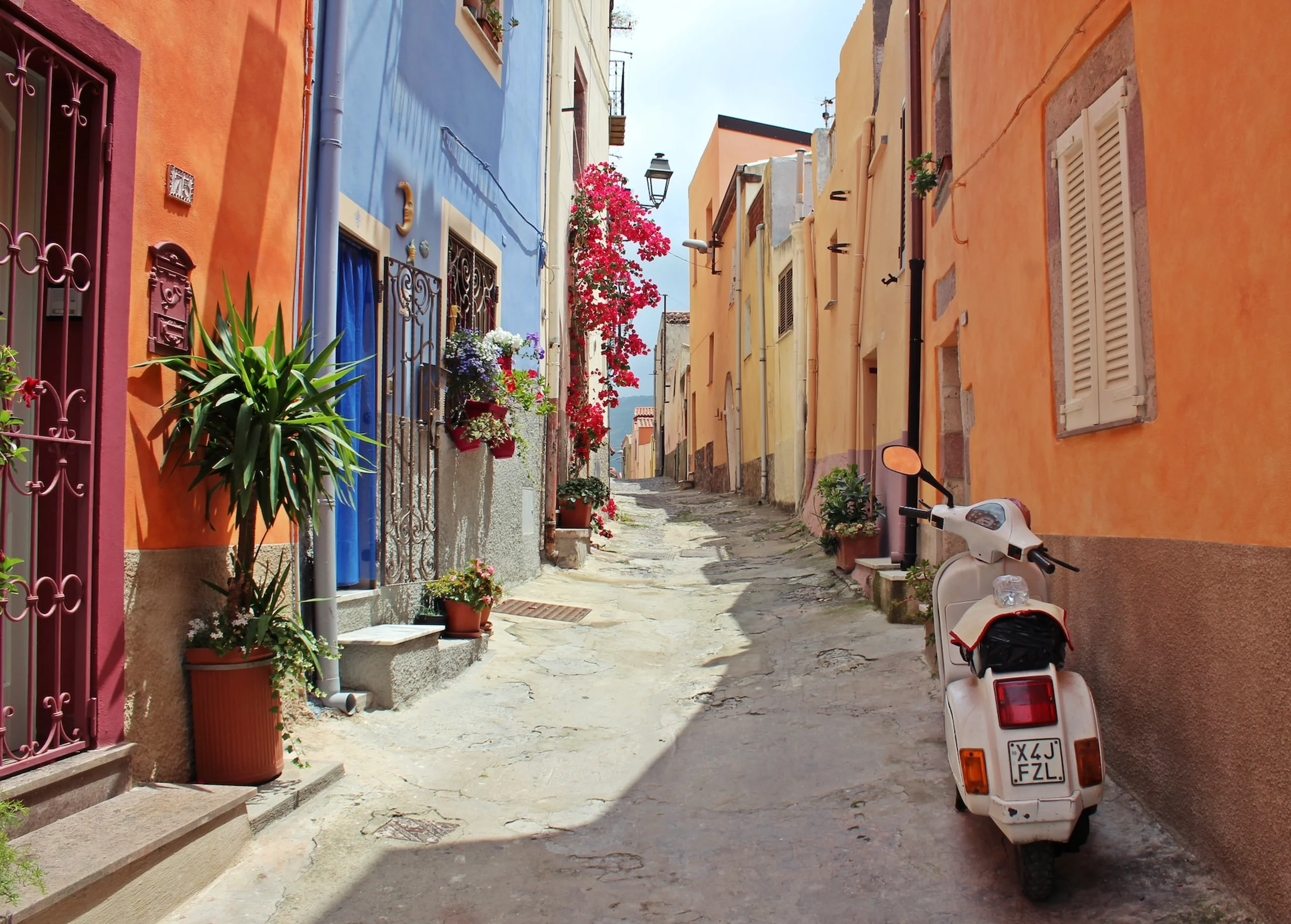 Narrow alley with orange and blue colourful buildings and parked vespa