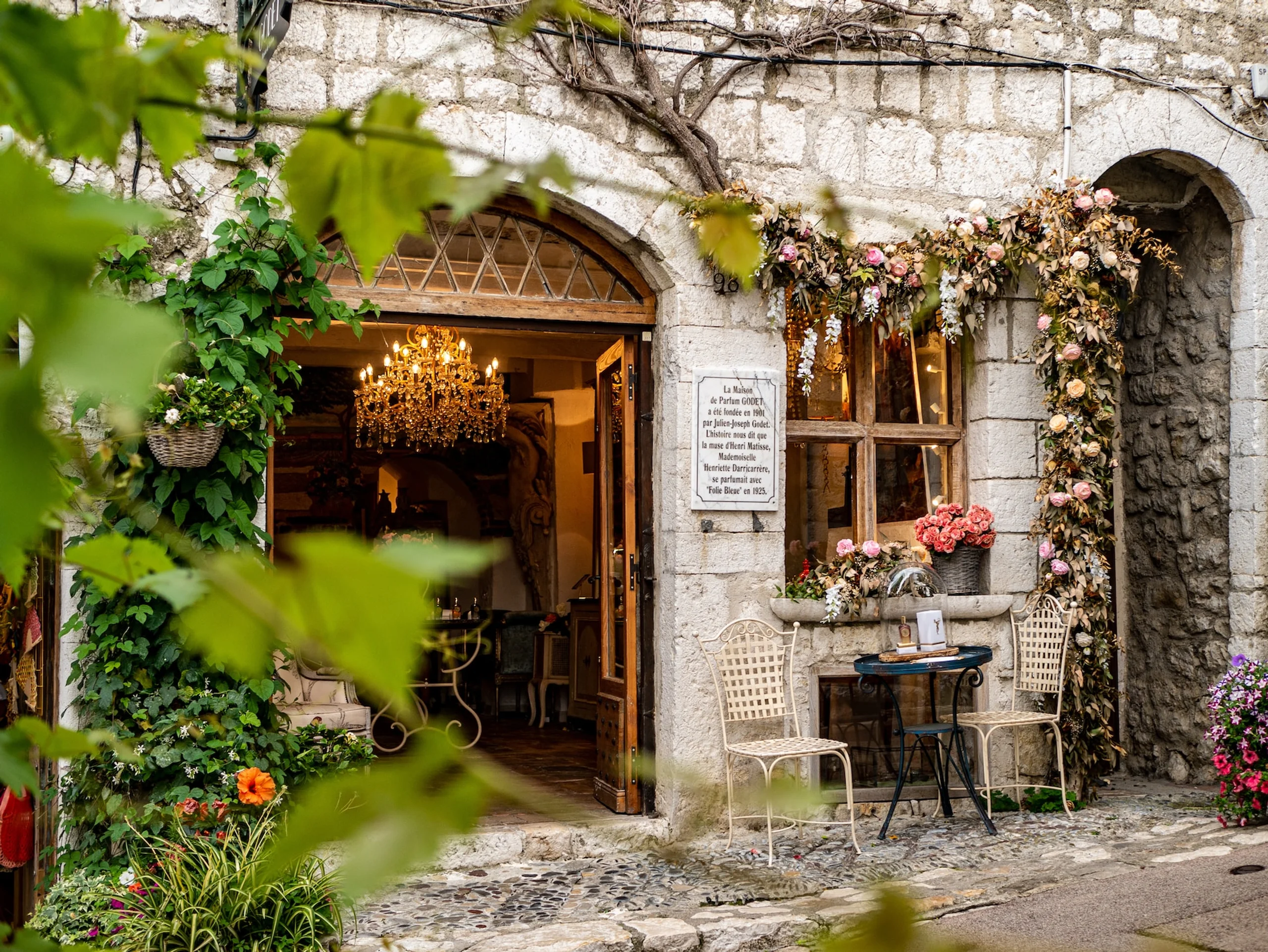 Cafe in a stone building with crystal chandelier and two seats and small table outside